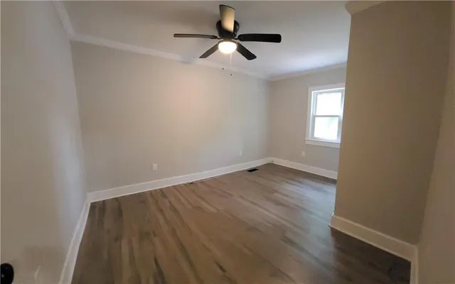 an empty room with wooden floor ceiling fan and windows