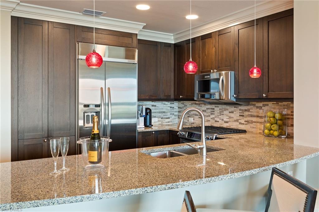 9115 Strada Place, Unit 5506 Naples, FL 34108 - Photo 15 of 46 Kitchen featuring stainless steel appliances, light stone countertops, dark brown cabinets, crown molding, and hanging light fixtures