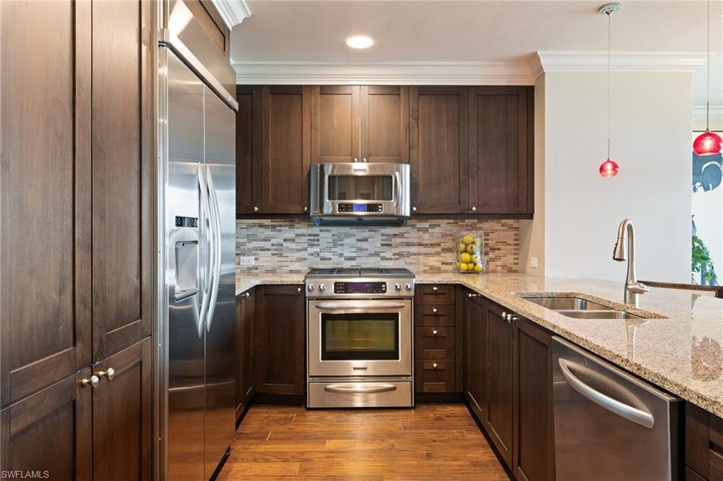 9115 Strada Place, Unit 5506 Naples, FL 34108 - Photo 16 of 46 Kitchen featuring stainless steel appliances, wood finished floors, dark brown cabinets, ornamental molding, and backsplash