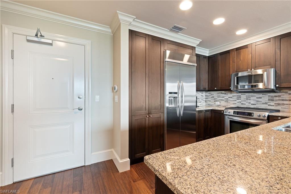 9115 Strada Place, Unit 5506 Naples, FL 34108 - Photo 26 of 46 Kitchen with stainless steel appliances, crown molding, light stone counters, dark wood-style floors, and tasteful backsplash