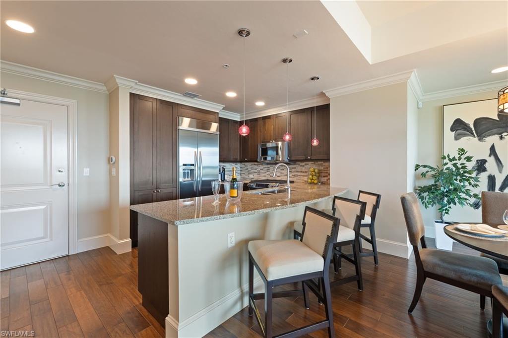 9115 Strada Place, Unit 5506 Naples, FL 34108 - Photo 6 of 46 Kitchen featuring light stone counters, stainless steel appliances, ornamental molding, dark wood-style flooring, and dark brown cabinets