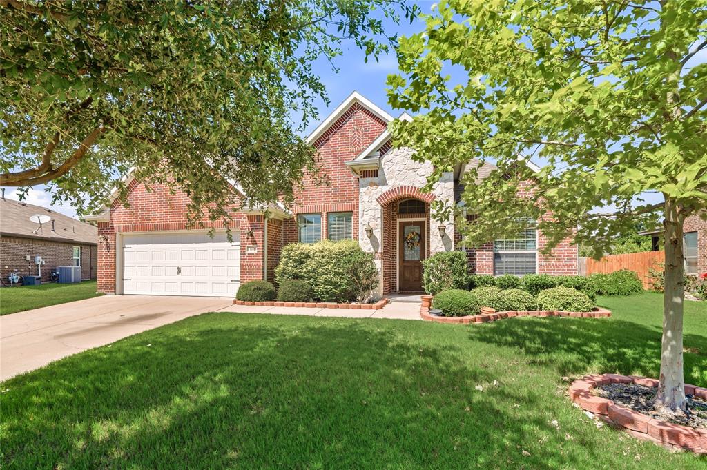 Brick and stone facade residence featuring an arched entryway, mature landscaping, an attached two-car garage, and a concrete driveway
