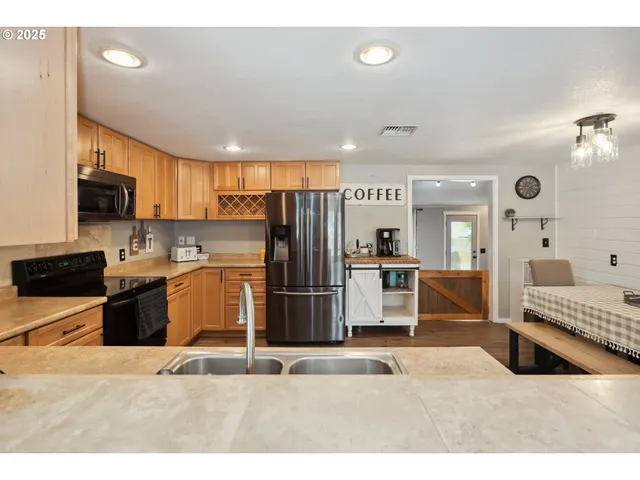 a kitchen with stainless steel appliances kitchen island granite countertop a refrigerator oven a sink dishwasher and white cabinets with wooden floor