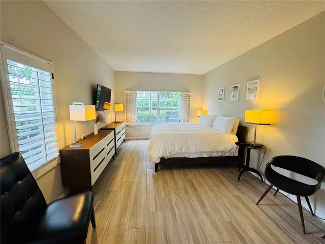 a spacious bedroom with a bed a table chair and a dresser next to a window