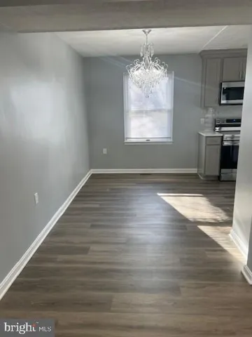 an empty room with wooden floor kitchen view and windows