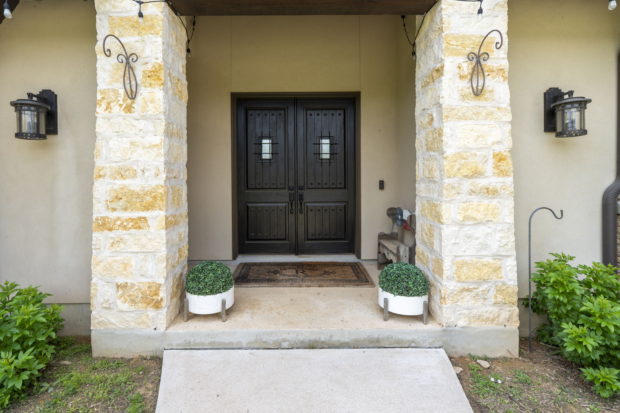 16202 Remuda Trail Buda, TX 78610 - Photo 3 of 40 The property features a grand entrance with double dark wood doors, flanked by stone pillars and wall-mounted light fixtures