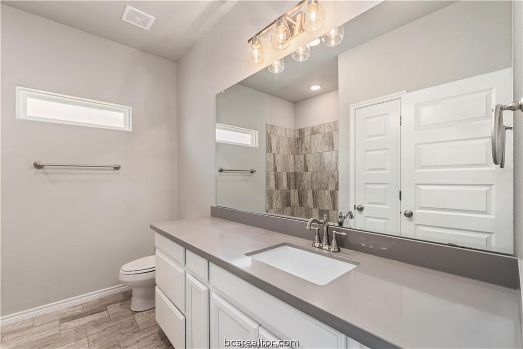 3185 Normandy Way Bryan, TX 77808 - Photo 13 of 16 a bathroom with a granite countertop sink a toilet and a large mirror