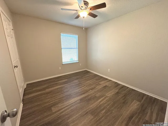 an empty room with wooden floor fan and windows