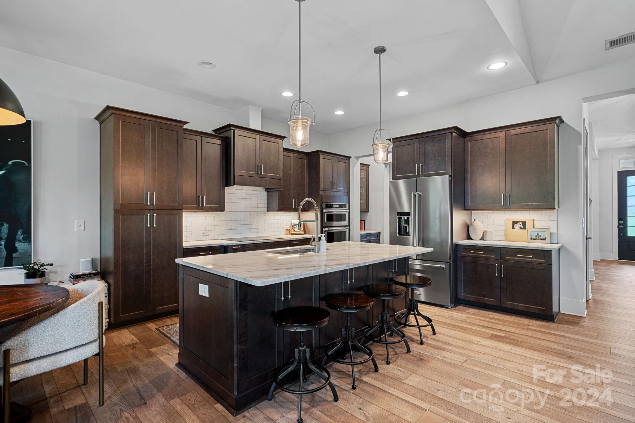 203 Webbed Foot Road Mooresville, NC 28117 - Photo 12 of 34 a kitchen with stainless steel appliances kitchen island granite countertop a refrigerator a stove a sink a dining table and chairs with wooden floor