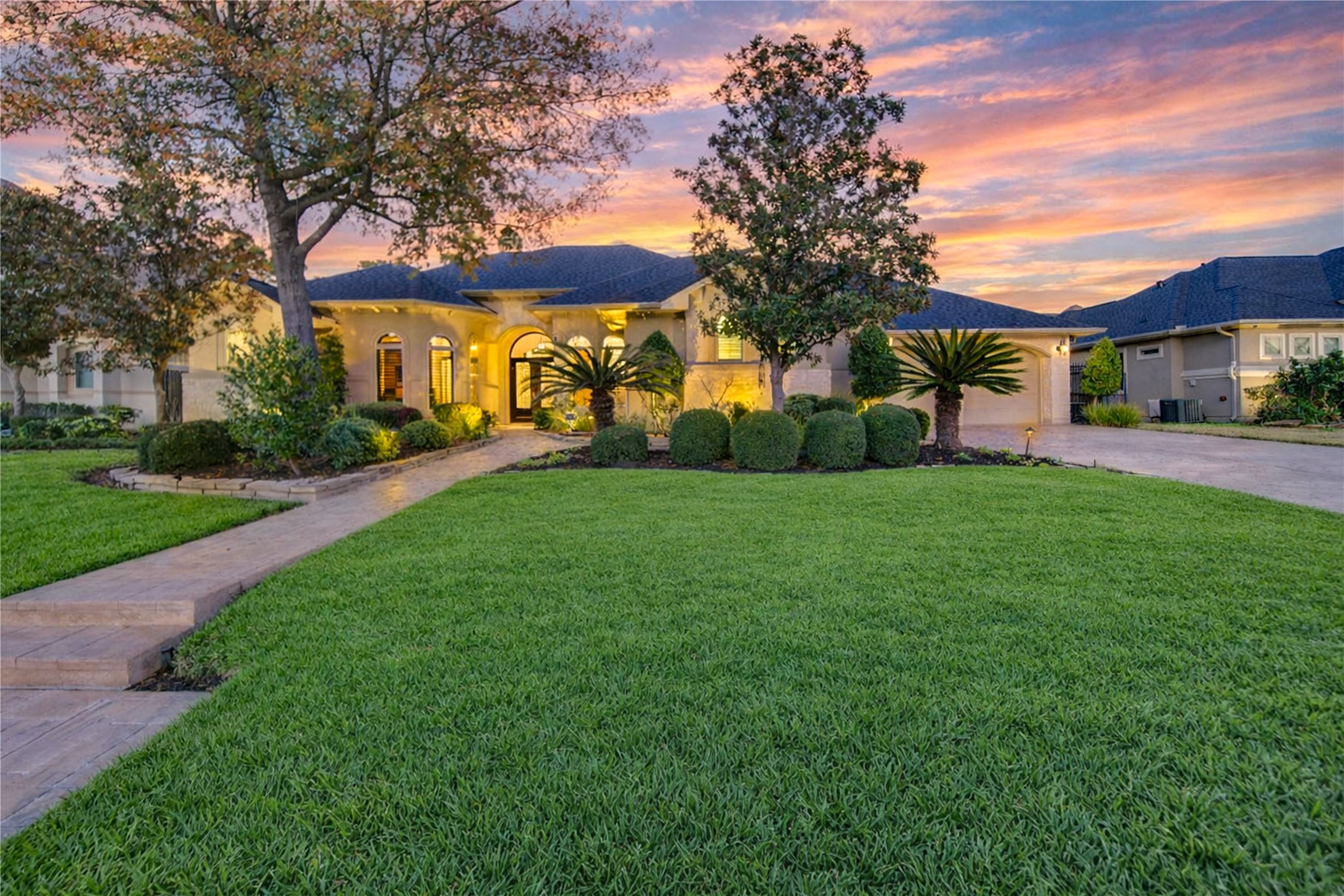 This stunning home features a beautifully landscaped front yard with a paved walkway leading to a grand entrance. Surrounded by manicured greenery and mature trees, the house boasts an elegant facade with arched windows and a welcoming atmosphere.