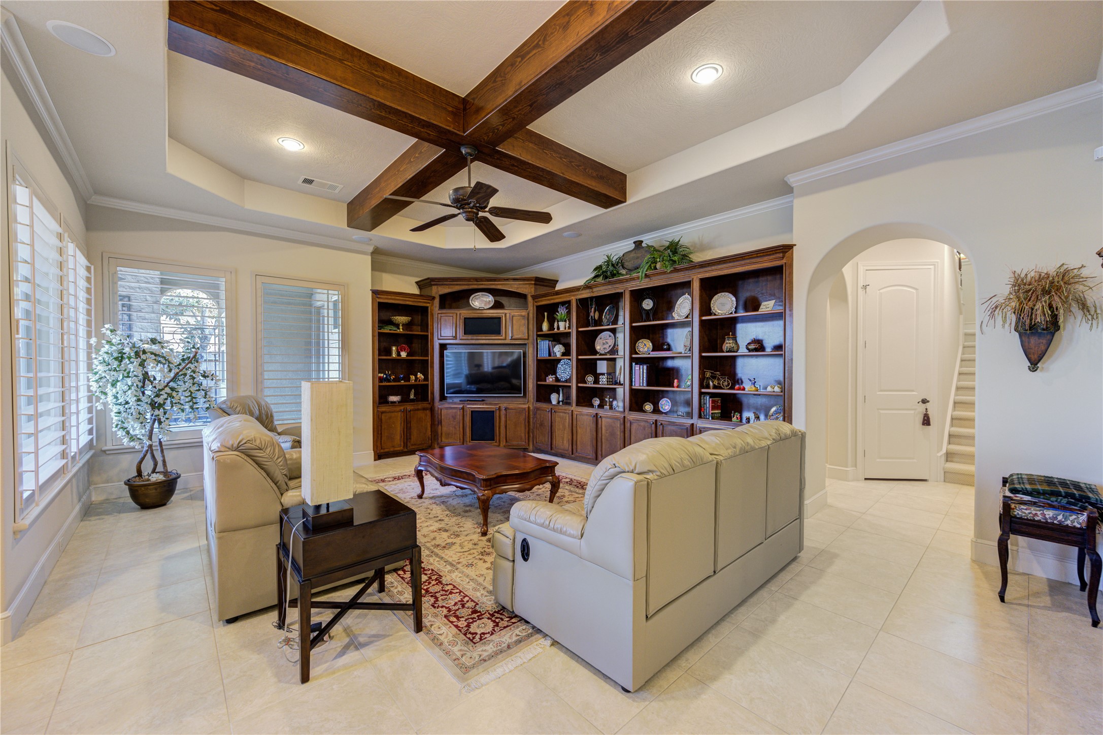 16618 Victoria Falls Lane Spring, TX 77379 - Photo 12 of 49 This spacious family room features elegant coffered ceilings with wooden beams, a cozy seating area, and a built-in entertainment center with ample shelving. Large windows provide plenty of natural light, and the neutral tile flooring complements the warm, inviting decor.