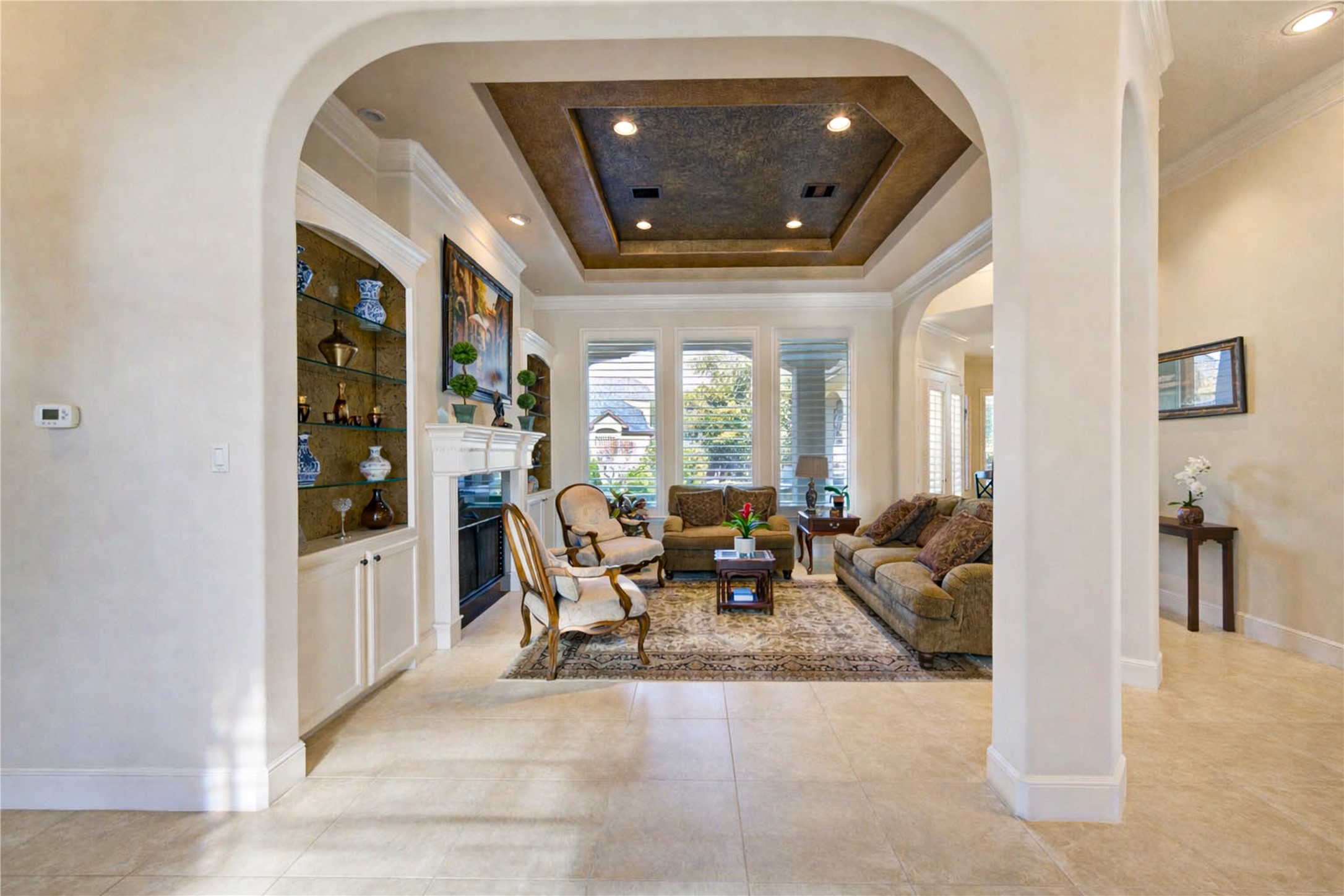 16618 Victoria Falls Lane Spring, TX 77379 - Photo 4 of 49 This elegant living room features high ceilings with recessed lighting, large windows for natural light, and an ornate fireplace. The space is framed by archways and includes built-in shelving, creating a sophisticated and inviting atmosphere.