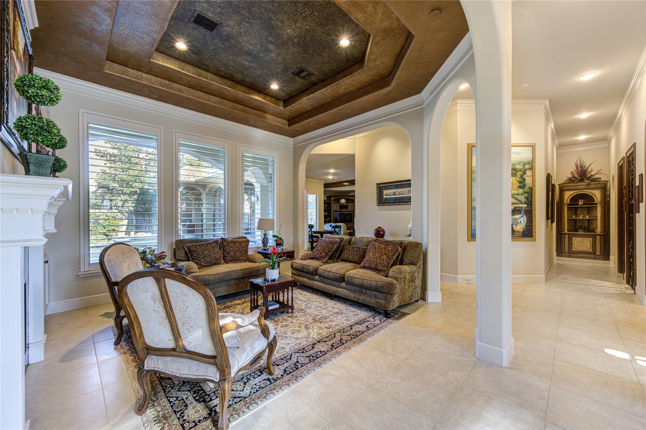 16618 Victoria Falls Lane Spring, TX 77379 - Photo 5 of 49 This beautiful living room features a coffered ceiling with recessed lighting, large windows with plantation shutters, and classic furnishings on a tile floor. The space is open and inviting, with archways leading to adjacent rooms and a cozy fireplace adding warmth.