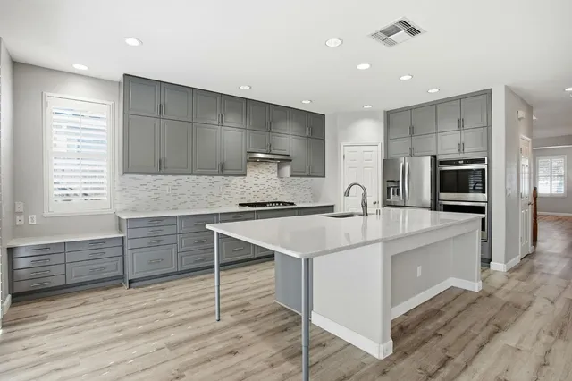 a kitchen with granite countertop a refrigerator oven a sink dishwasher and white cabinets with wooden floor