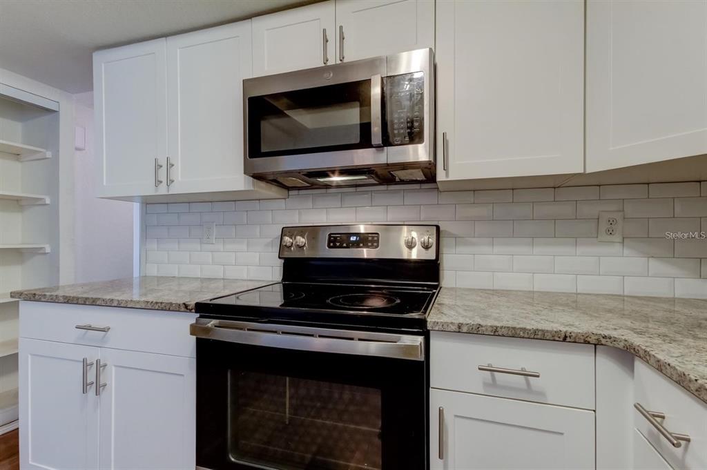 7144 Fairfax Drive Port Richey, FL 34668 - Photo 15 of 53 a kitchen with stainless steel appliances granite countertop stove top oven microwave and cabinets
