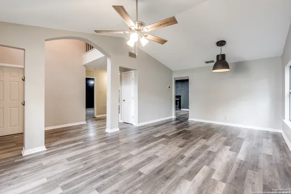 a view of an empty room with wooden floor and a ceiling fan