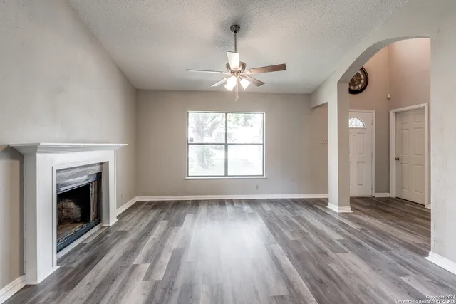 an empty room with wooden floor fireplace and windows