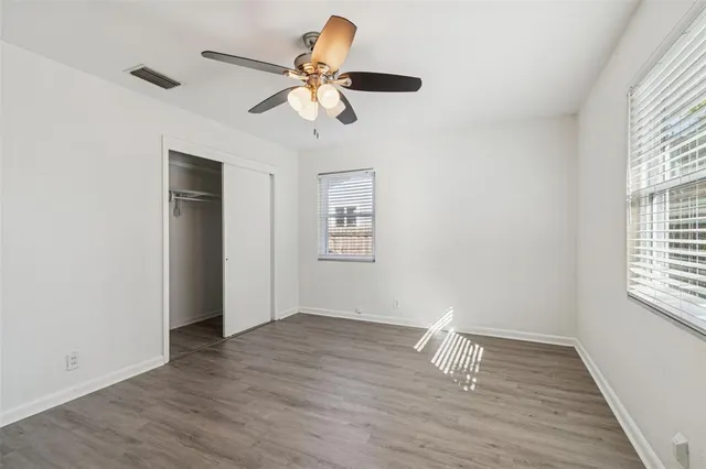 an empty room with wooden floor fan and windows