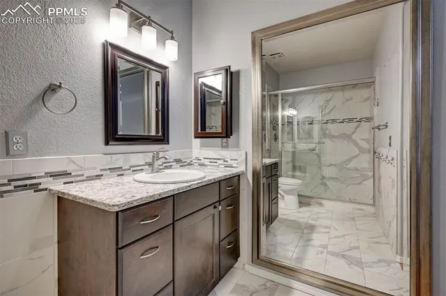 a bathroom with a granite countertop sink a toilet a mirror and shower