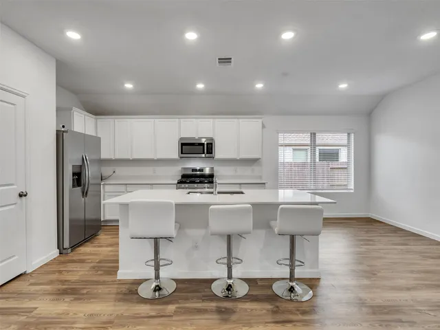 a kitchen with stainless steel appliances granite countertop a sink a stove a refrigerator and white cabinets with wooden floor