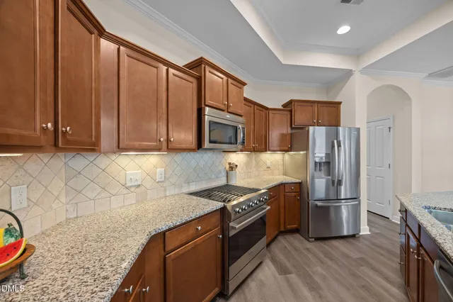 a kitchen with stainless steel appliances granite countertop a refrigerator a stove and a sink with wooden floors