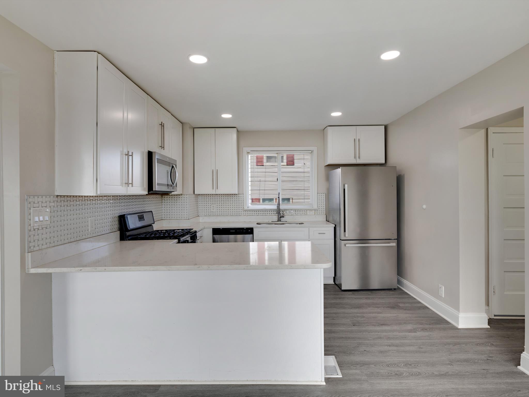 4129 5th Street Baltimore, MD 21225 - Photo 13 of 52 a kitchen with a refrigerator a stove top oven and a center island with wooden floor