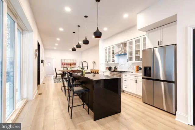 a kitchen with stainless steel appliances kitchen island granite countertop a refrigerator a oven a stove and white cabinets with wooden floor