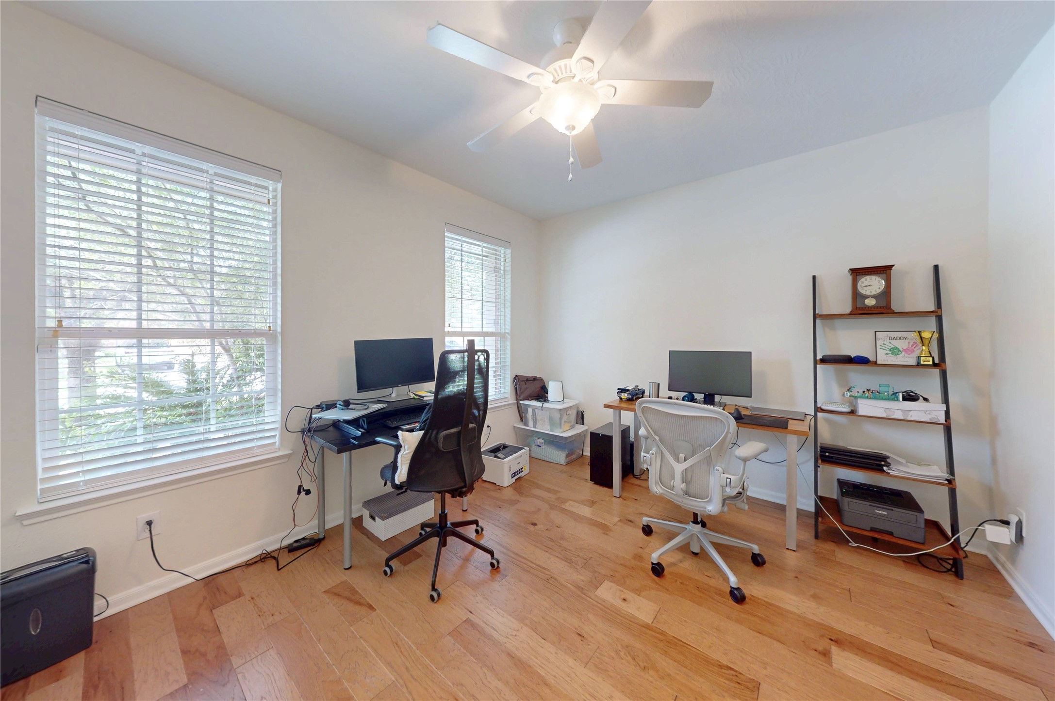 17402 Rainer Valley Lane Humble, TX 77346 - Photo 7 of 33 This bright home office features hardwood floors, a ceiling fan, and two large windows providing ample natural light. It includes space for dual workstations and a shelving unit for storage, creating an ideal work-from-home environment.
