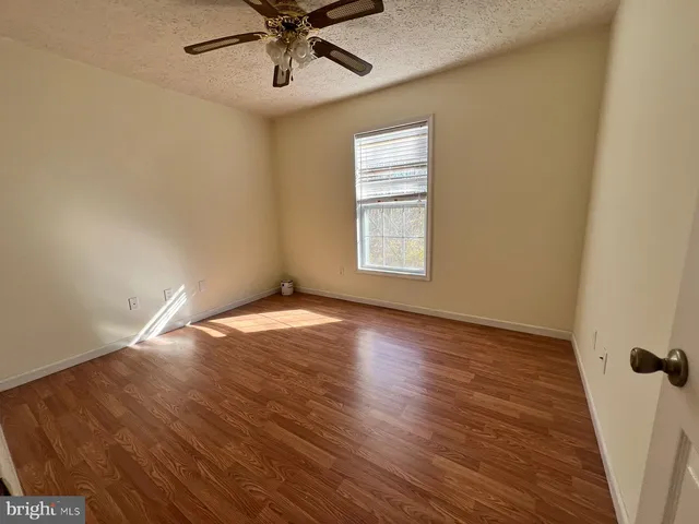 an empty room with wooden floor fan and windows