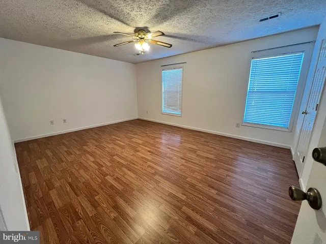 an empty room with wooden floor fan and windows
