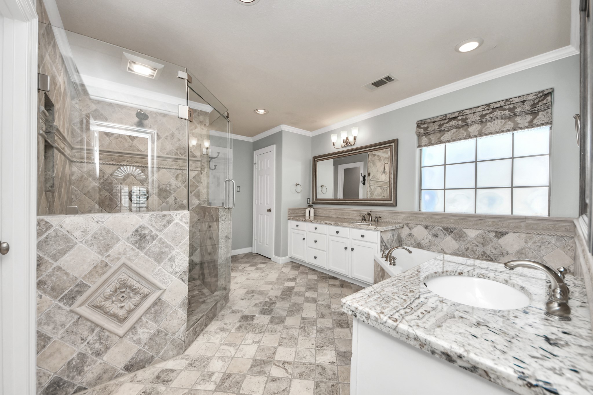 710 Jackson Hill Street Houston, TX 77007 - Photo 23 of 31 This spacious bathroom features a large glass-enclosed shower with decorative tile, dual sinks with granite countertops, ample cabinetry, and a frosted window for natural light.