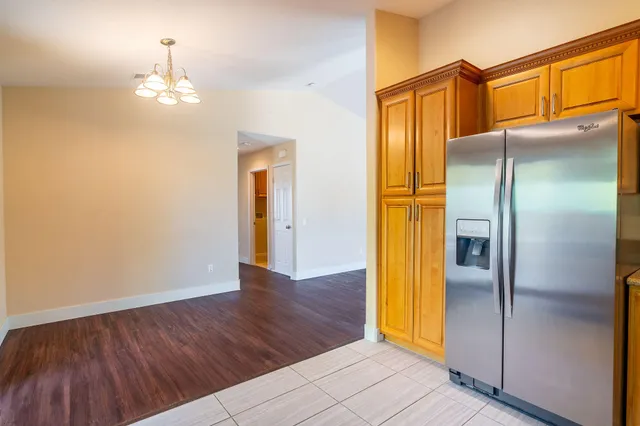 a view of a refrigerator in kitchen and an empty room with wooden floor