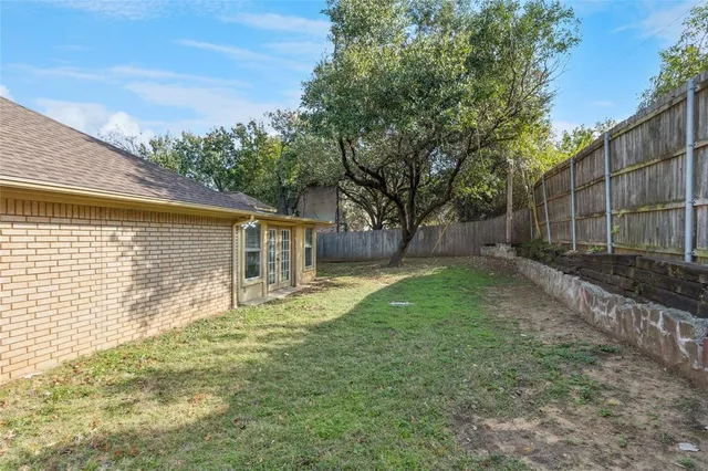 a backyard of a house with large trees and wooden fence