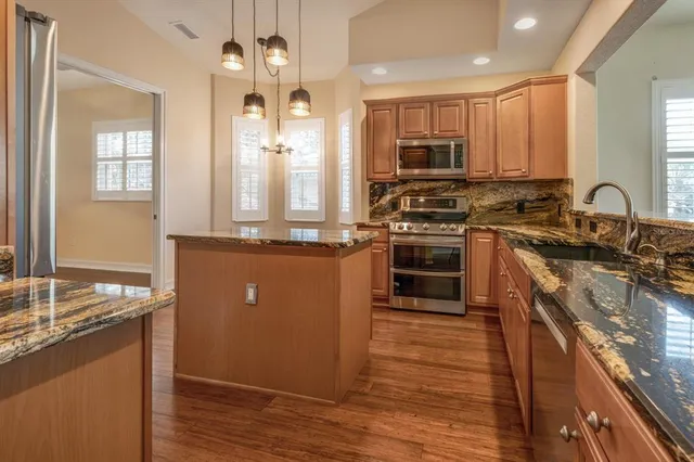 a kitchen with kitchen island granite countertop a stove top oven a sink and dishwasher with wooden floor