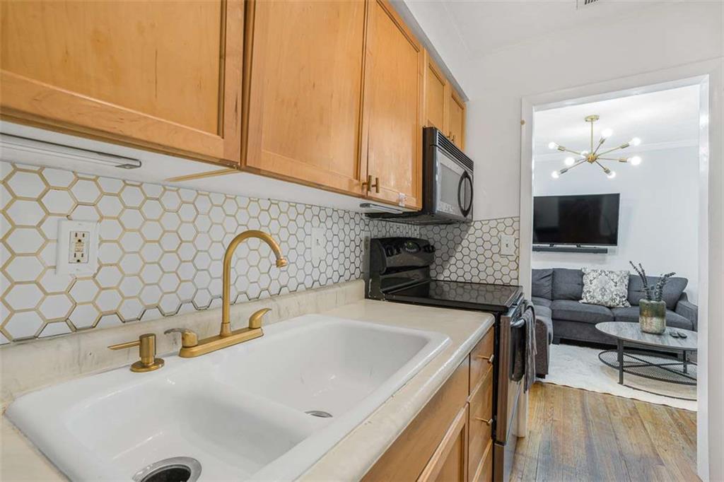 1150 Collier Road Northwest, Unit 25D Atlanta, GA 30318 - Photo 9 of 21 a kitchen with stainless steel appliances a sink a stove and a microwave with wooden floor