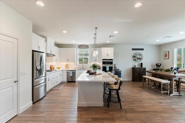 a large kitchen with stainless steel appliances a table chairs refrigerator and cabinets