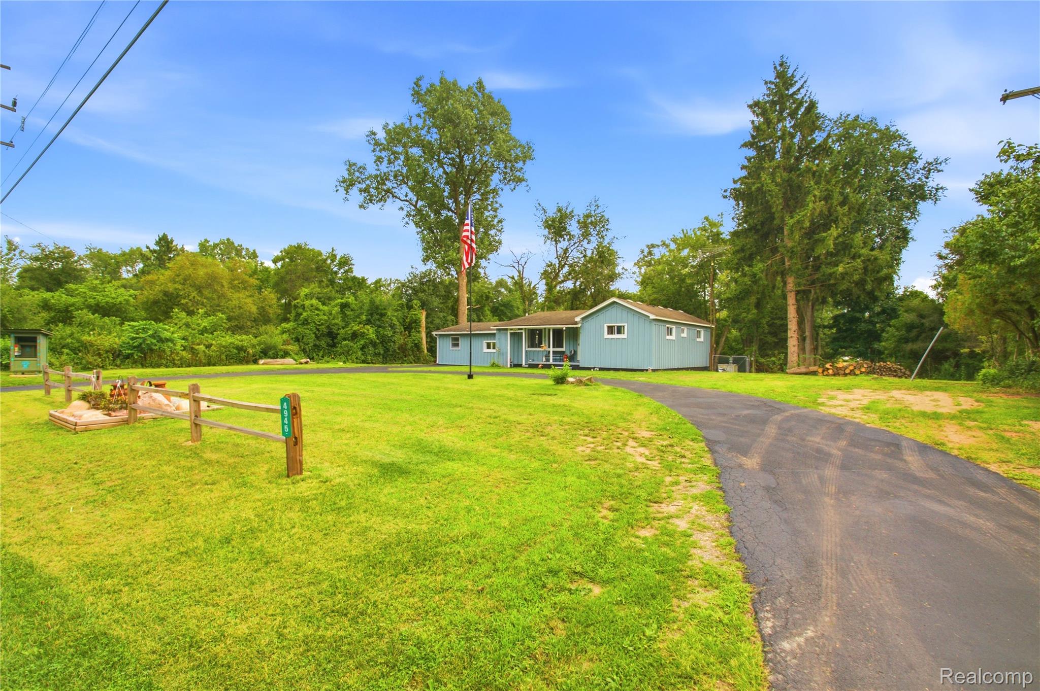 4945 Miller Road Ann Arbor, MI 48103 - Photo 32 of 42 Light blue exterior with white trim, covered front porch, paved driveway, expansive green lawn, and mature trees