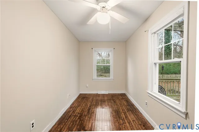 an empty room with wooden floor fan and windows