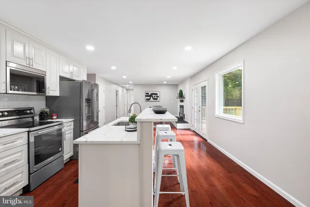 a living room with stainless steel appliances kitchen island granite countertop a sink a stove a microwave a refrigerator cabinets and wooden floor