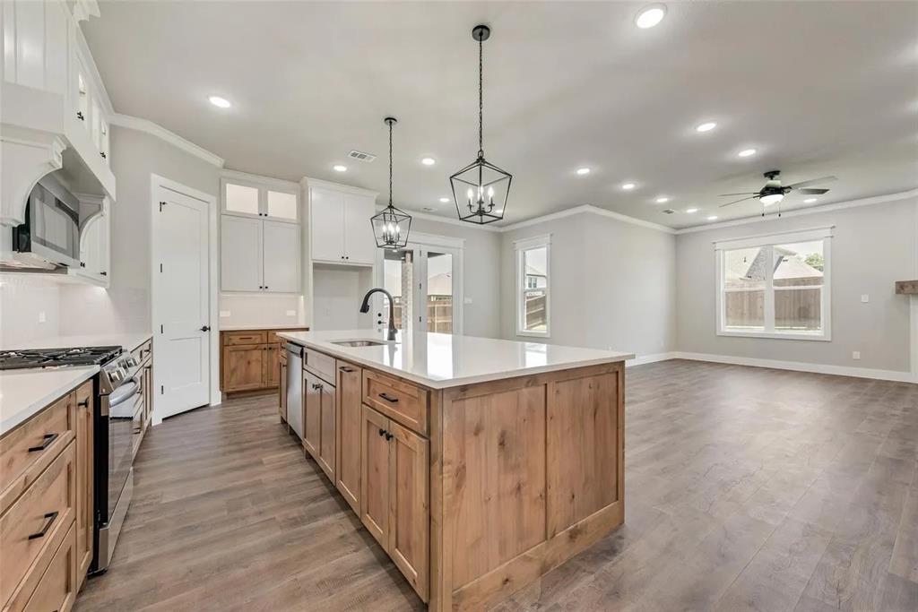 1327 Selby Road Van Alstyne, TX 75495 - Photo 32 of 32 Two tone kitchen featuring two tone cabinetry, stainless steel appliances, ornamental molding, open floor plan, and an island with sink
