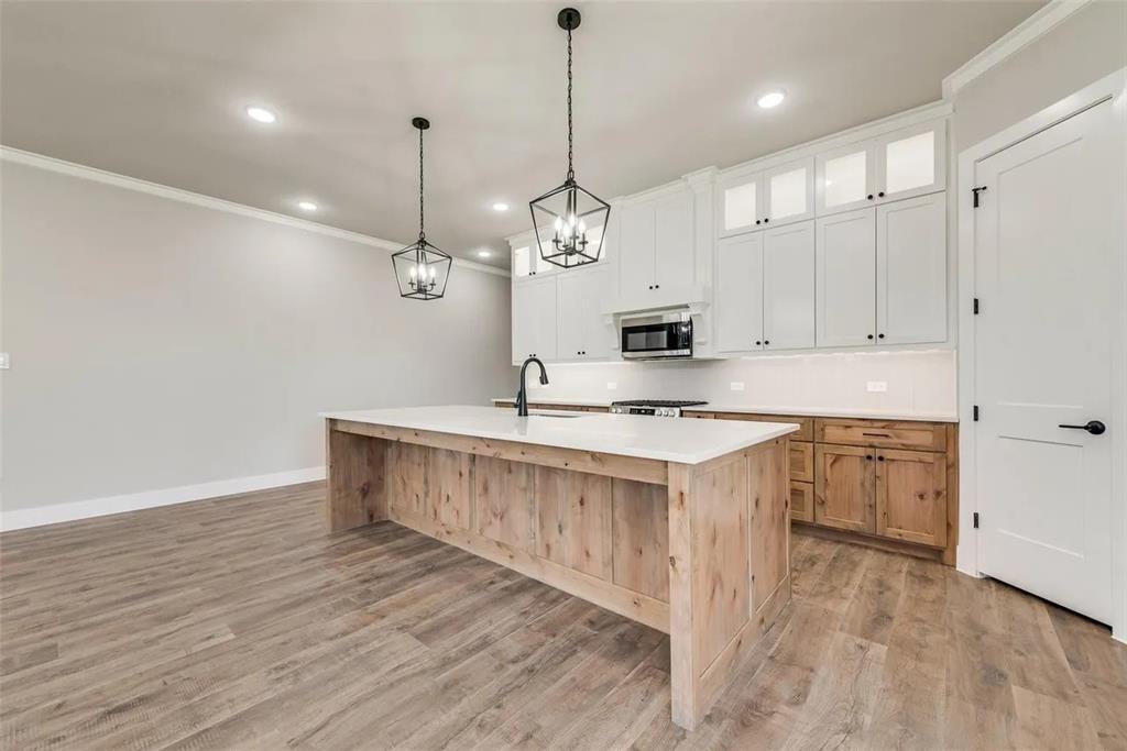 1327 Selby Road Van Alstyne, TX 75495 - Photo 3 of 32 Kitchen featuring two tone cabinets, ornamental molding, an island with sink, glass insert cabinets, and light wood-style flooring