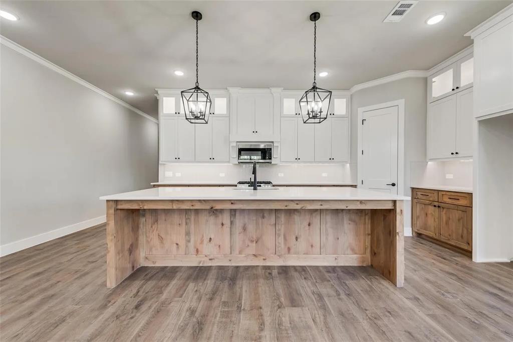 1327 Selby Road Van Alstyne, TX 75495 - Photo 6 of 32 Kitchen featuring decorative backsplash, a large island with sink, dual tone cabinets, stainless steel microwave, and light wood-style flooring