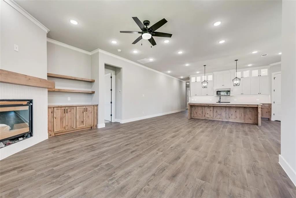 1327 Selby Road Van Alstyne, TX 75495 - Photo 8 of 32 Unfurnished living room with crown molding, recessed lighting, a ceiling fan, a glass covered fireplace, and light wood-style floors