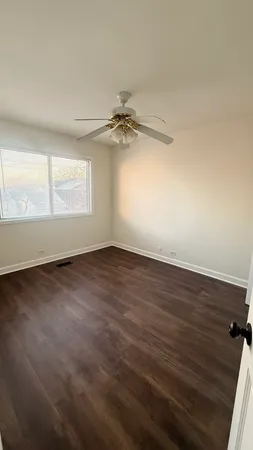 an empty room with wooden floor fan and windows