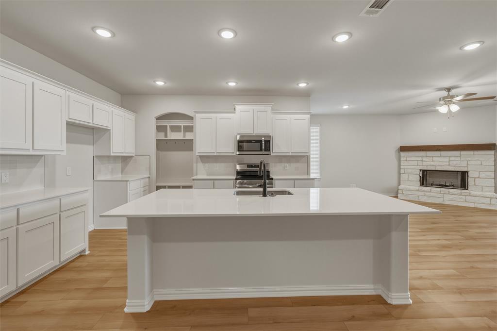 1325 Frio Drive Springtown, TX 76082 - Photo 8 of 24 Open-concept kitchen featuring an expansive island with an undermount sink, white cabinetry, stainless steel appliances, and wood-finish flooring