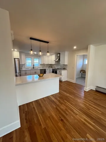 a kitchen with stainless steel appliances kitchen island granite countertop a refrigerator a stove and a sink with wooden floor