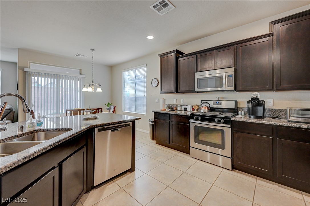 6970 Motley Road Las Vegas, NV 89178 - Photo 7 of 52 Kitchen with island, espresso cabinets, stainless steel appliances, recessed lighting, granite countertops, pantry, ceramic tile flooring