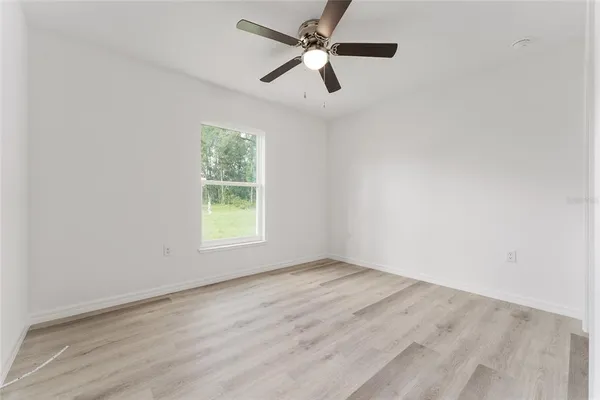 an empty room with wooden floor ceiling fan and windows