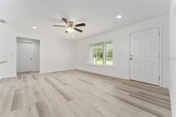 an empty room with wooden floor ceiling fan and windows