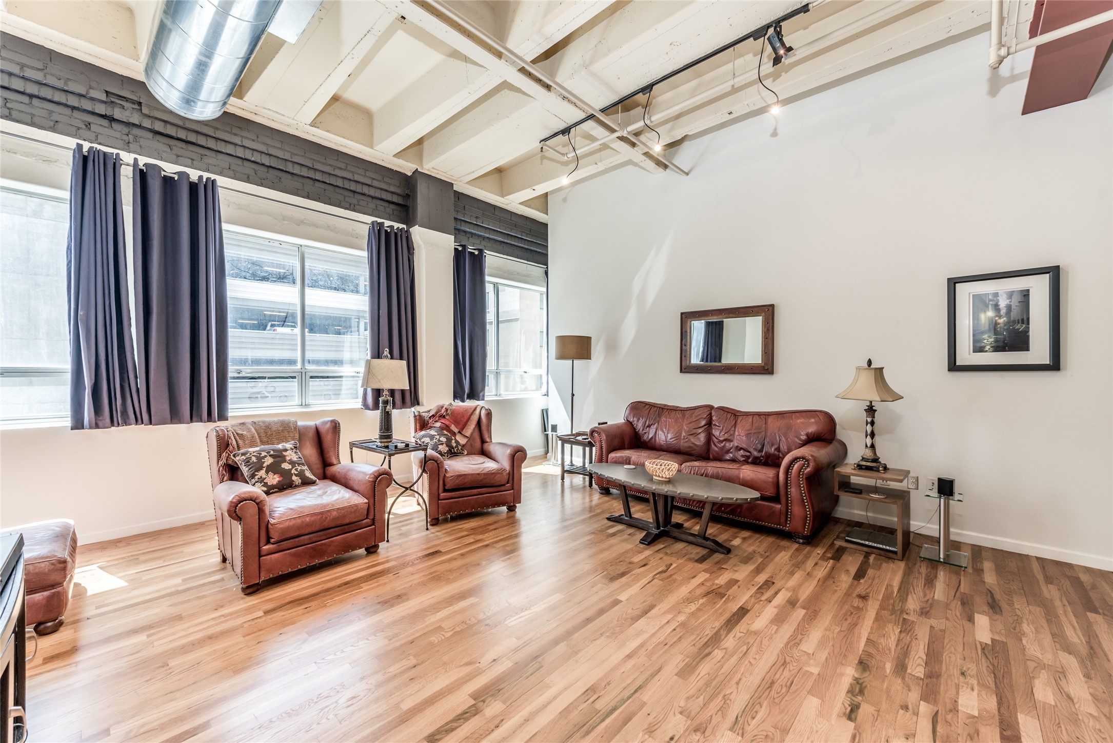 705 Main Street, Unit 215 Houston, TX 77002 - Photo 8 of 36 This spacious living room features a modern industrial vibe with exposed ductwork, high ceilings, and large windows for ample natural light.